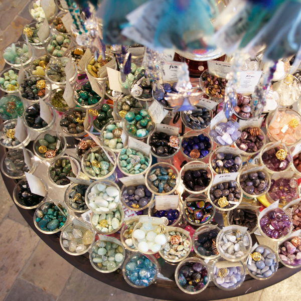lots of small glass bowls filled with tumbled stones of all different colours displayed on a glass table